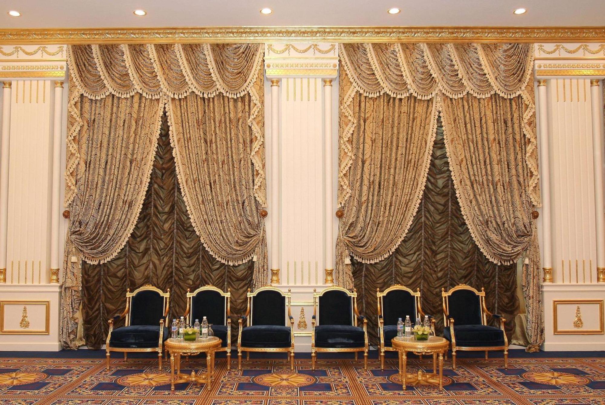 Grand Regency Doha, Trademark Collection By Wyndham Екстер'єр фото The photo shows an elegantly decorated interior space. There are two sets of opulent curtains on the walls, featuring rich fabrics with ornate designs and gold accents. The curtains are paired with decorative tiebacks. In front of the curtains, there