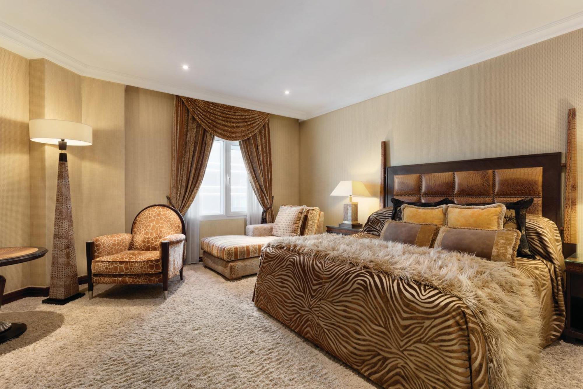 Grand Regency Doha, Trademark Collection By Wyndham Екстер'єр фото The photo shows a stylishly decorated bedroom. The focal point is a large bed dressed in fabrics with a rich, textured appearance, possibly featuring a zebra print or similar design. On either side of the bed, there are small bedside lamps. 

Adjacen
