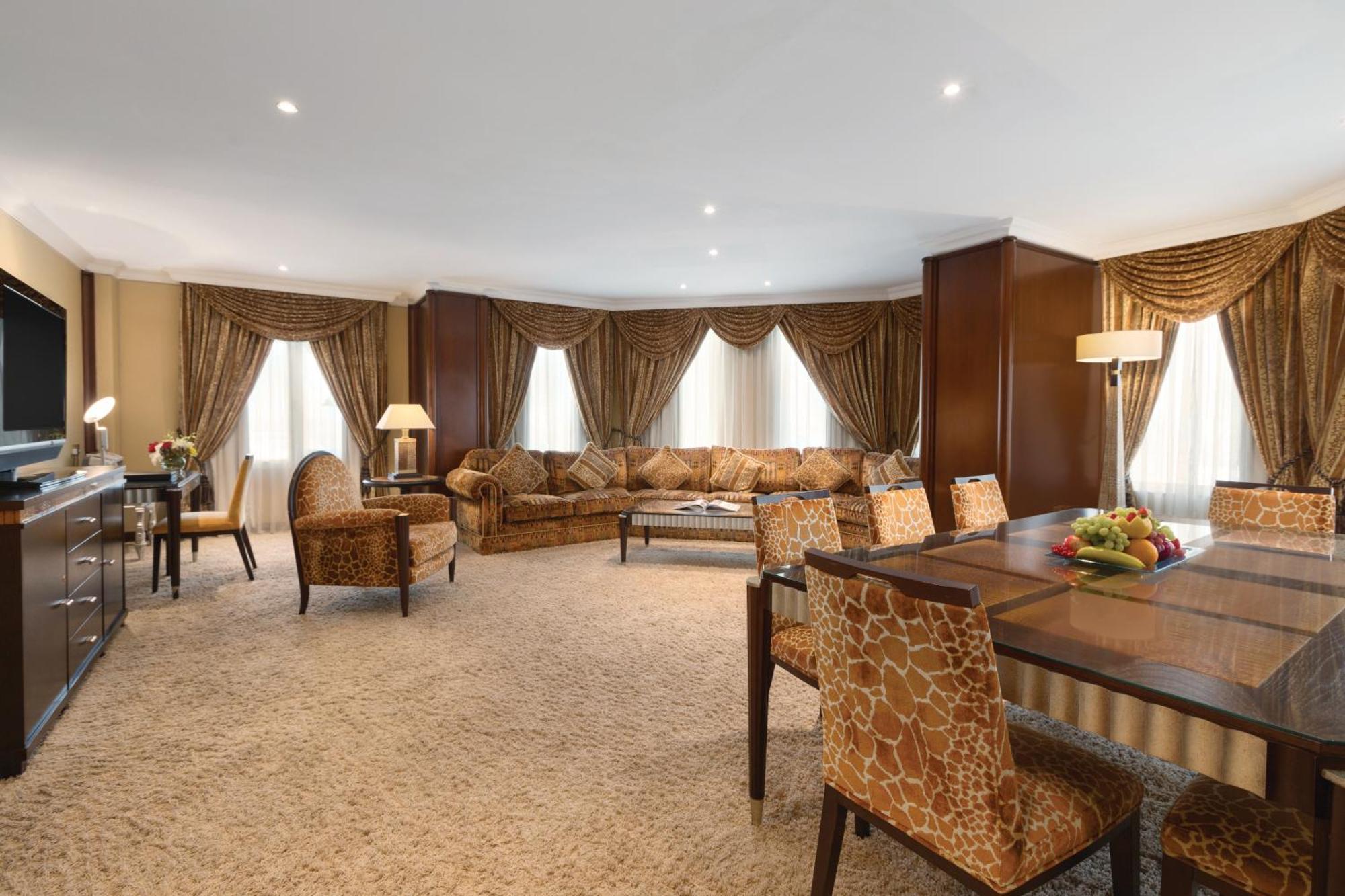 Grand Regency Doha, Trademark Collection By Wyndham Екстер'єр фото The photo shows a spacious and elegantly designed living area. There are large windows dressed with luxurious curtains, allowing natural light to fill the room. The seating arrangement features a comfortable sofa with various cushions and several sty