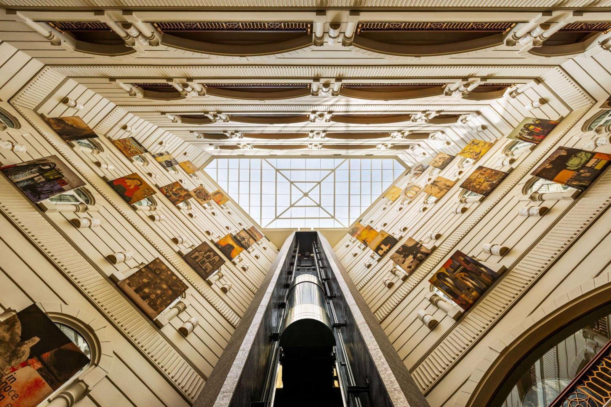 Grand Regency Doha, Trademark Collection By Wyndham Екстер'єр фото The photo shows an interior view of a building, captured from a low angle looking upwards. The architectural design features a tall, open space with walls adorned with various artworks. In the center, there is a glass ceiling that allows natural ligh