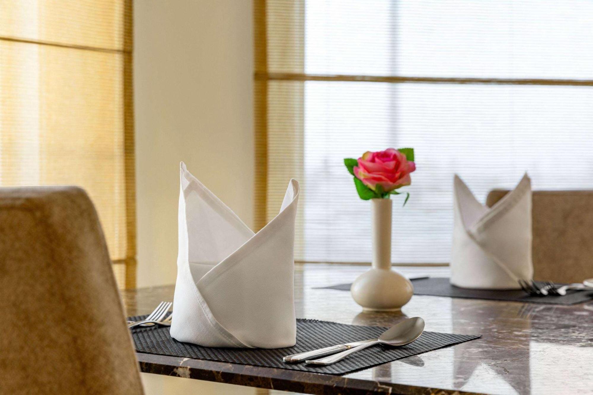 Grand Regency Doha, Trademark Collection By Wyndham Екстер'єр фото The photo shows a neatly arranged dining table. On the table, there are two cloth napkins folded in a decorative way, one at each place setting. Silverware, including a knife and fork, is placed next to each napkin. In the center of the table, there 